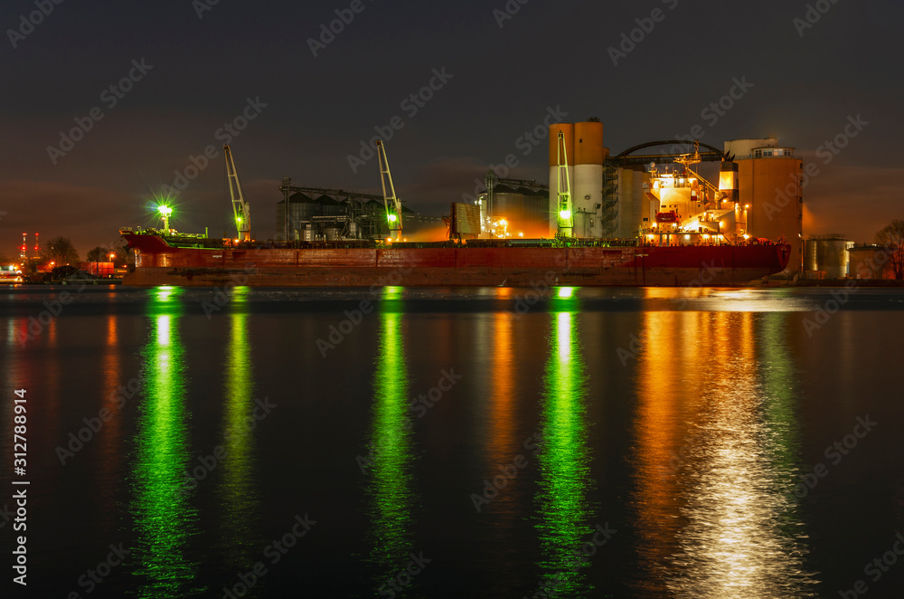 Duży statek zacumowany w porcie, krajobraz przemysłowy nocą. 