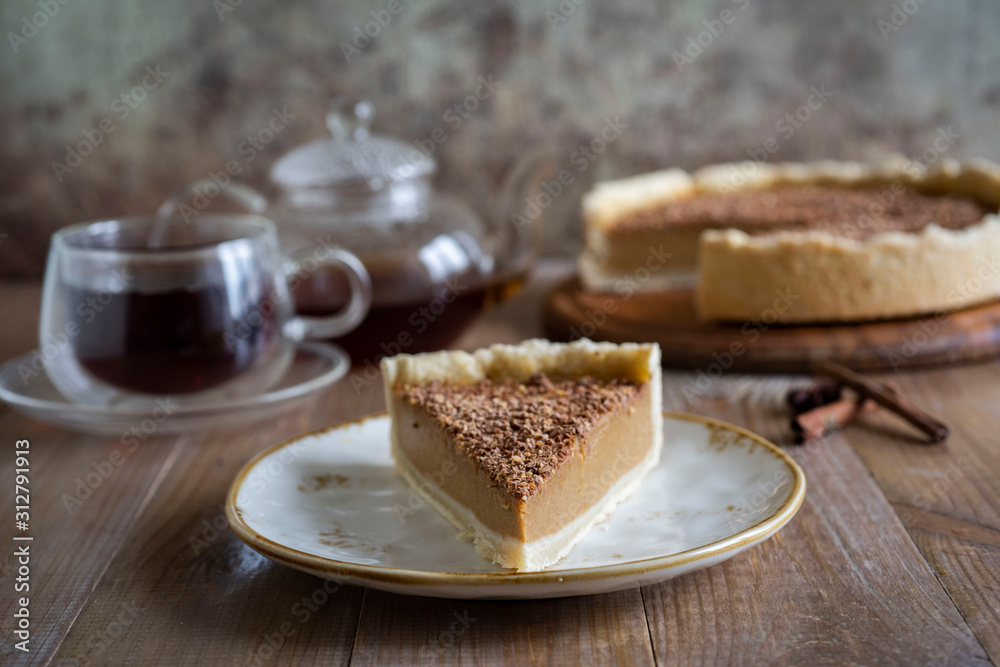A delicious slice of pumpkin cheesecake on a vintage plate on a wooden table. In the background is a pumpkin cheesecake and a glass Cup of hot tea A delicious slice of pumpkin cheesecake on a vintage plate on a wooden table. In the background is a pumpkin cheesecake and a glass Cup of hot tea