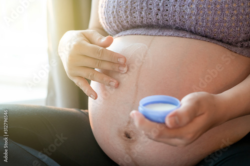 Big belly of pregnant woman applying a skin care lotion on her stomach.  Healthcare and healthy mother concept. Pregnantcy woman. photo