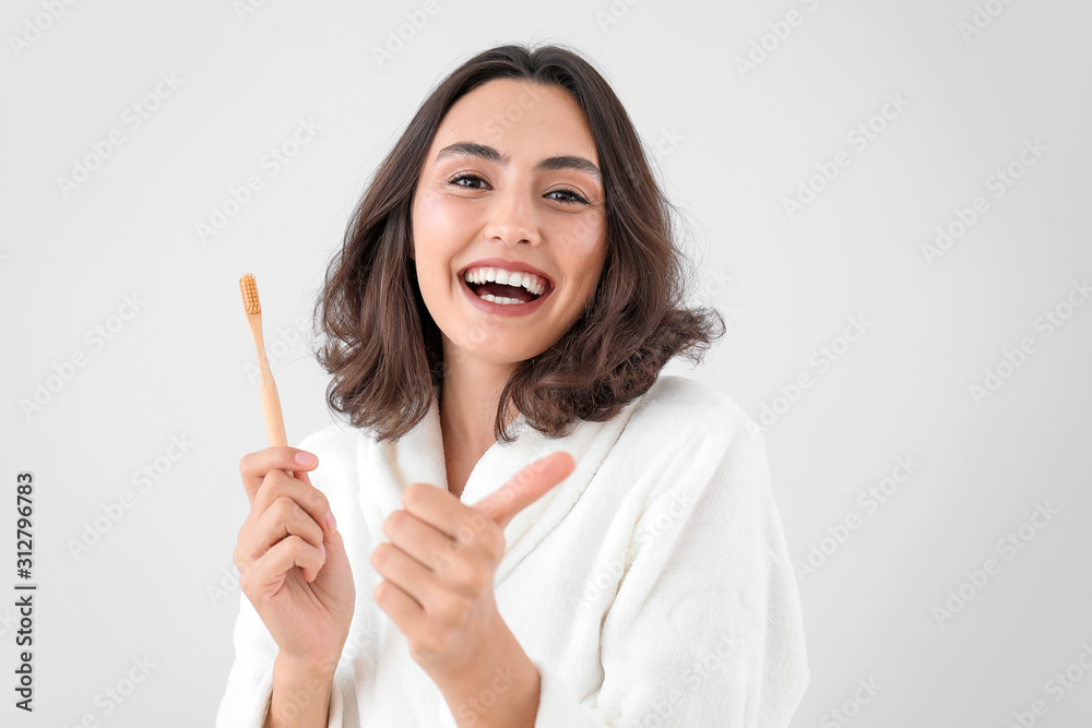 Beautiful young woman with toothbrush showing thumb-up gesture on light background Beautiful young woman with toothbrush showing thumb-up gesture on light background