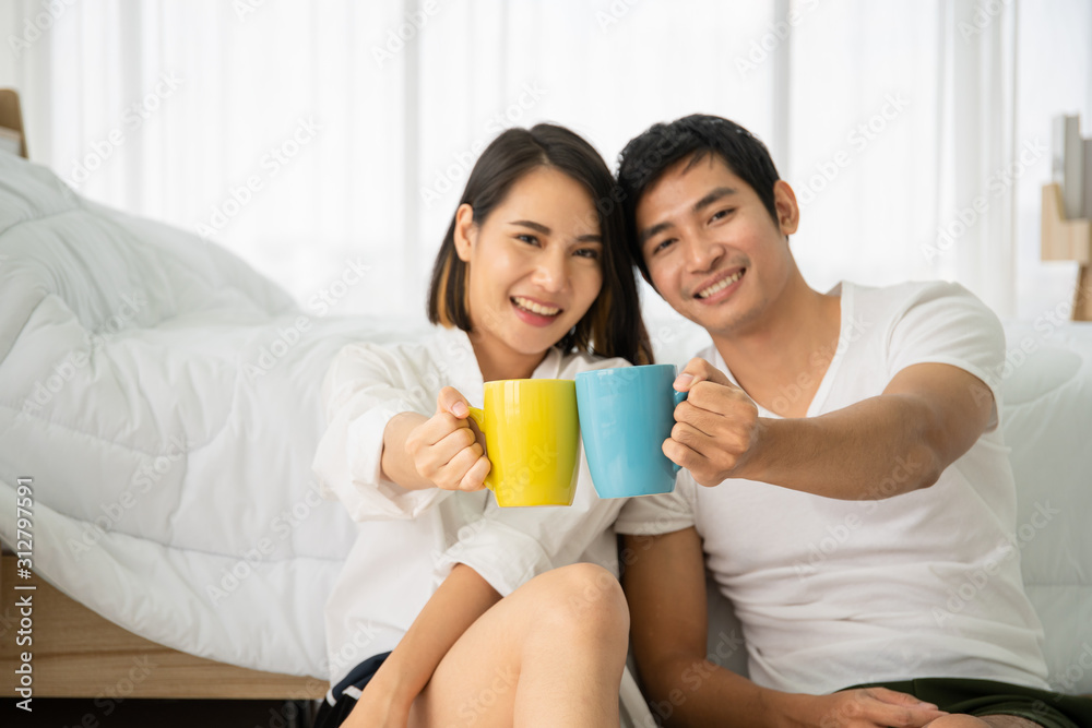 Asian young couple enjoying together with coffee in the morning in badroom, concept of leisure, couple, relationship and valentine. Photograph with copy space. Focused on the coffee mugs.