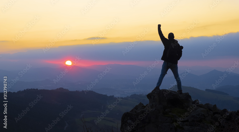 Mountaineer on top celebrating success with the sun at sunset over Gipuzkoa from Mount Jaizkibel, Euskadi