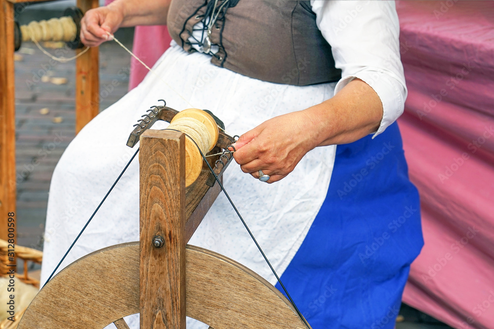 Craftswoman using an old spinning wheel to turn wool into yarn. Hands of a  woman demonstrating traditional wool spinning on an old spinning wheel.  Spinning on a spinning wheel. Spinning wheel. Stock