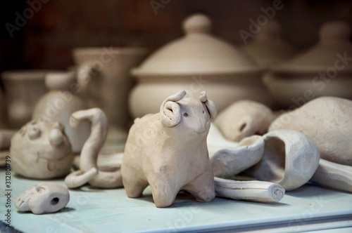 Clay toy sheep ready for roasting in the oven in the master’s workshop on the background of other fresh white clay products.