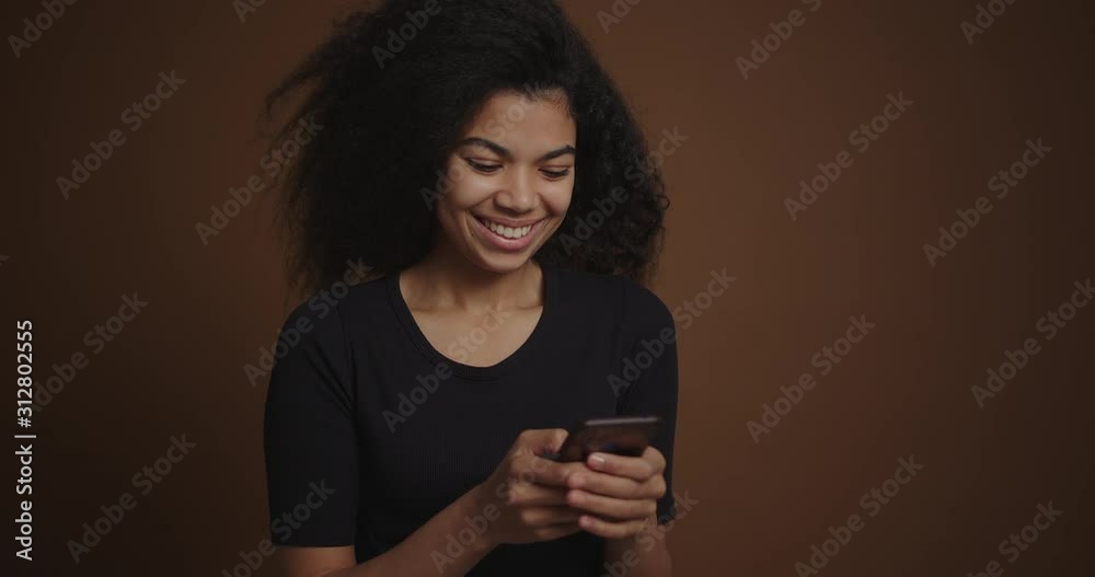 African american girl messaging on her cell phone on brown background African american girl messaging on her cell phone on brown background