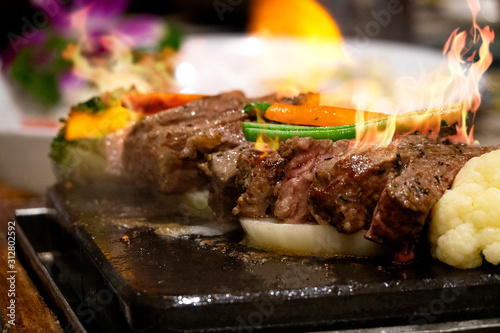 Close up beef on hot dish on fire with vegetables. Live cooking in the restaurant. photo