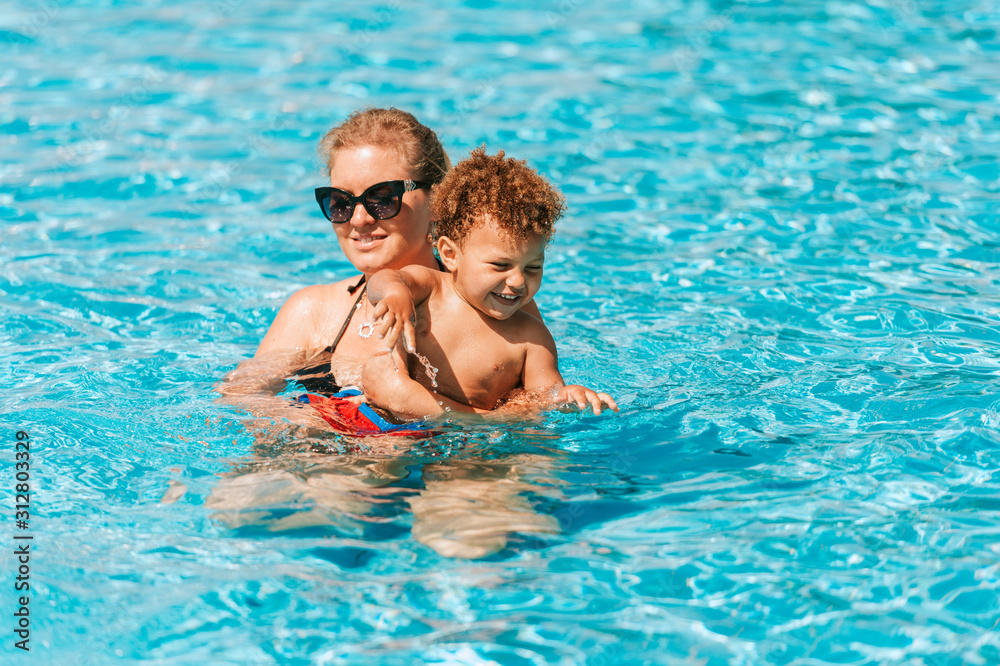 Happy young mother playing with kid in pool on a hot summer day