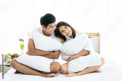 Funny and romantic Asian couple' portrait in bedroom with natural light from window, concept of relationship between husband and wife and being a family.