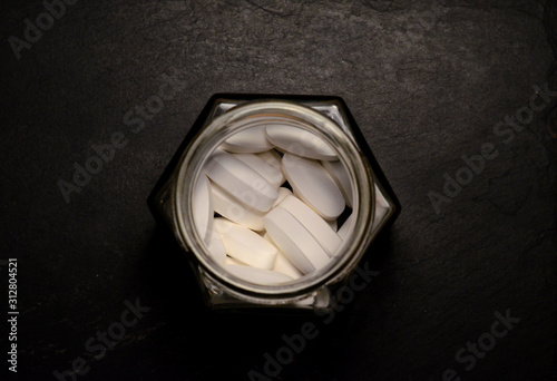 oblong white pills in glass hexagonal jar
