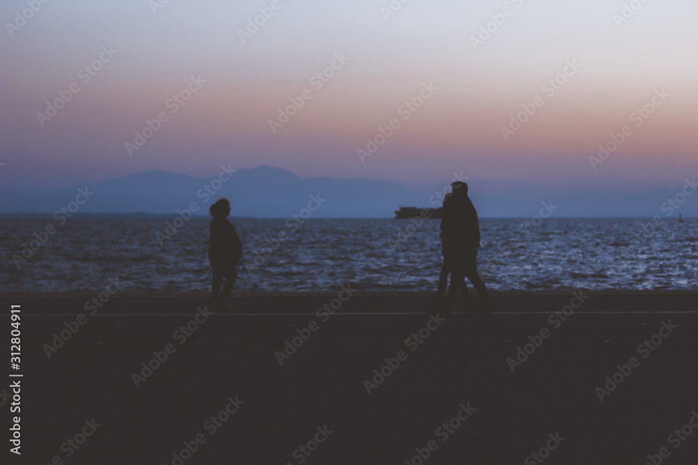 people silhouette promenade in evening time on dock waterfront district with dark sea horizon background with empty copy space for your text here