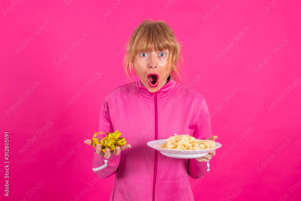 woman with stress expression looking at measuring tape and plate of pasta or hydrates with sportswear isolated on pink background woman with stress expression looking at measuring tape and plate of pasta or hydrates with sportswear isolated on pink background