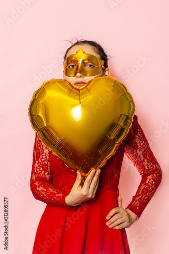 Woman wearing masquerade mask and holding heart shaped air ballon. Valentines Day, Birthday, Anniversary, Festive, Ball celebration concepts © Golib Tolibov