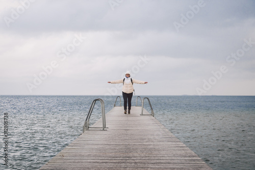 Concept of freedom relaxation. woman relaxing on pier. Woman hiker backpacker with backpack on sea wooden pier goes forward. Emotion of happiness, freedom and future