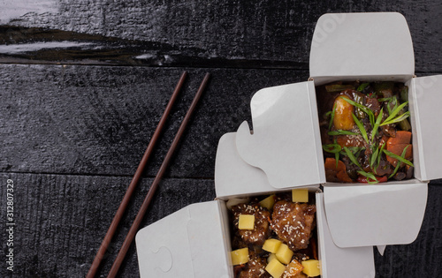 Delicious wok noodles box container with udon and chicken on wooden table. Chinese and asian takeaway fast food,flat lay