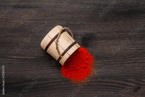 Magyar (Hungarian) brilliant red sweet paprika powder. Traditional seasoning for cooking national food. Wooden keg, black wooden background photo