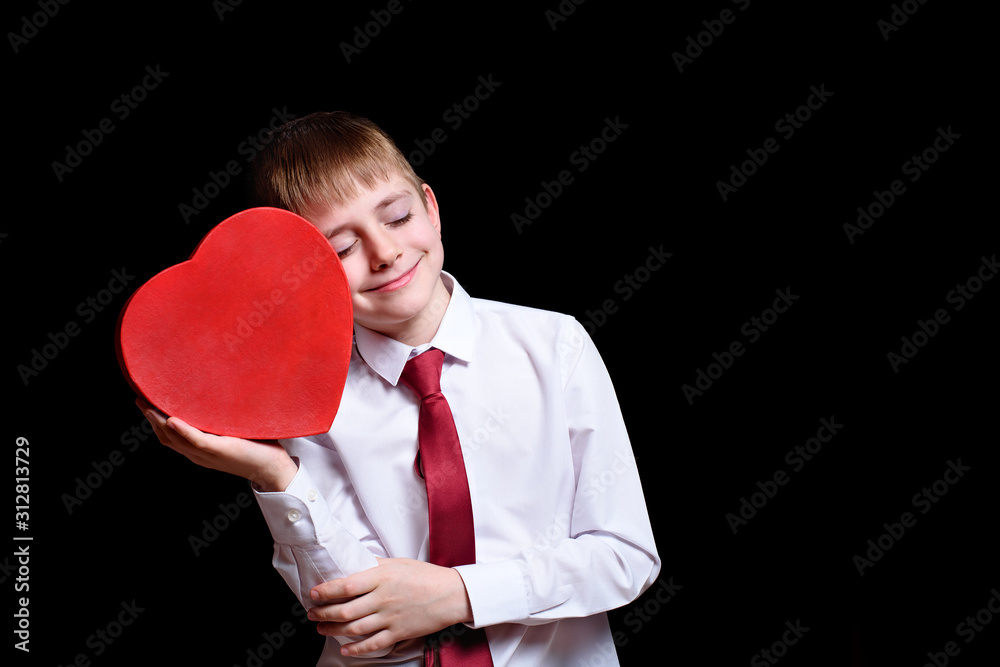 Closed eyes boy leans against his cheek red heart shape box on a dark background Closed eyes boy leans against his cheek red heart shape box on a dark background
