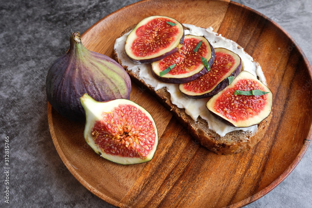Rye and spelt sourdough toast with creamy yogurt and feta cheese, fresh figs with honey, next to pieces of fresh figs with cinnamon on a large wooden plate. Rye and spelt sourdough toast with creamy yogurt and feta cheese, fresh figs with honey, next to pieces of fresh figs with cinnamon on a large wooden plate.