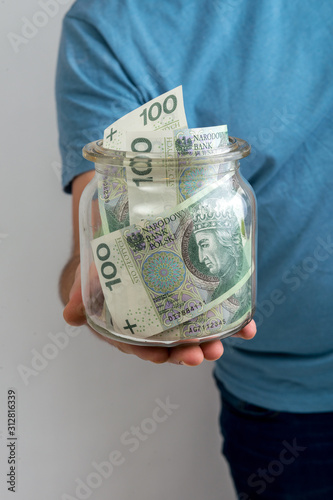 Polish zloty banknotes inside the jar holding by a man hand. Man hand holding jar with Polish money inside