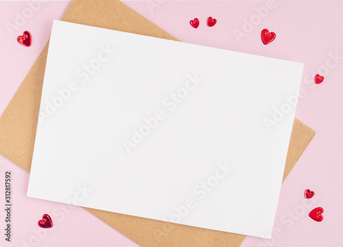Minimalistic card mockup with envelope, postcard, pen, red hearts on  pink background. Flat lay, top view, copy space. Valentines day concept.
