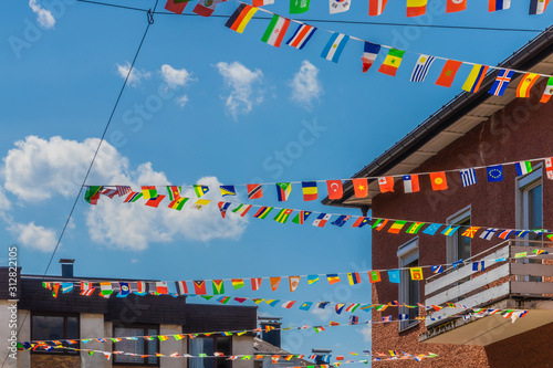 Colorful paper flags of different countries hanging on wires, blue sky and residential buildings in the background. International travel concept.