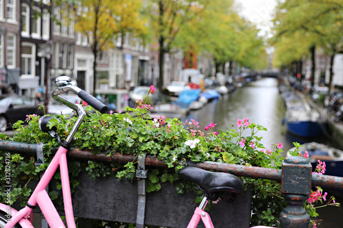Slika na platnu Focus on the pink bike with a short depth of field with the canal blurry in the background in Amsterdam