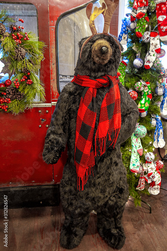 Fun faux bear standing tall in country store with red plaid scarf welcoming vistors during Christmas holiday. photo