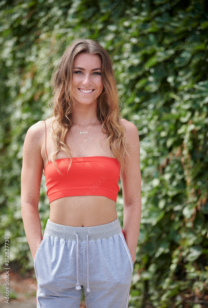 Sexy young brunette woman poses in red or coral tank top near an urban ivy covered wall - summer fashion Sexy young brunette woman poses in red or coral tank top near an urban ivy covered wall - summer fashion