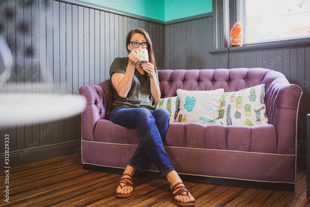 Obraz premium Young woman in cafe on couch drinking cup of coffee