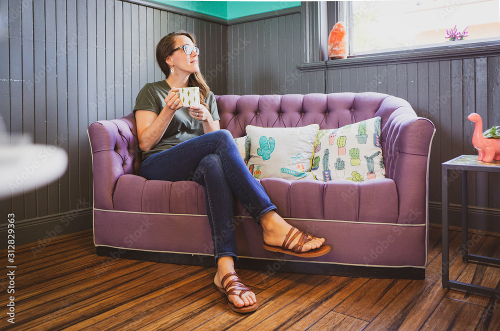 Obraz premium Young woman in cafe on couch drinking cup of coffee