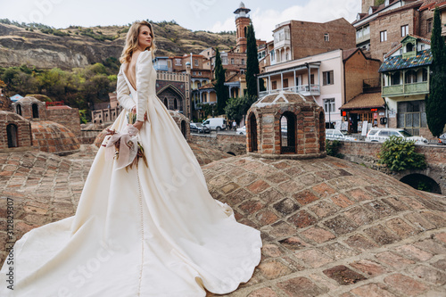 incredibly charming bride poses for a photo in a sophisticated wedding dress on the background of old Georgian city Tbilisi