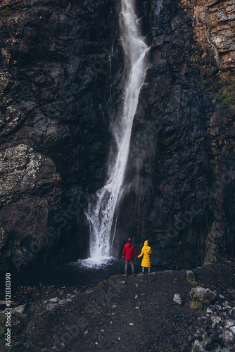 Beautiful waterfall in Georgia. Couple in raincoats looking on scenic high waterfall holding hands. concept of tourism and extreme travel