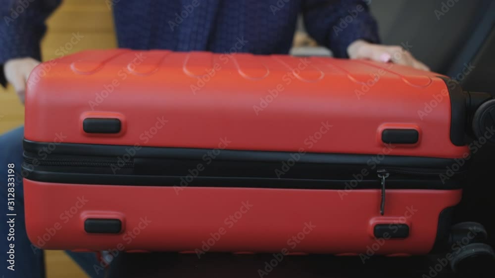 Closeup woman covers the big red suitcase in the lobby of the airport and puts him on the floor. Closeup woman covers the big red suitcase in the lobby of the airport and puts him on the floor.