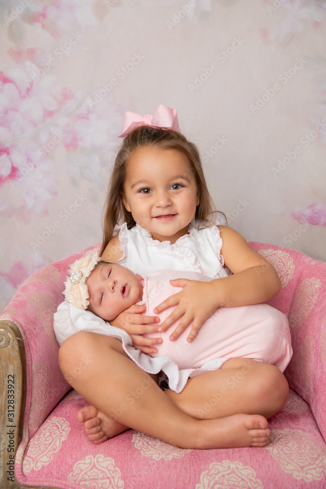 3 year old big sister holding her newborn little sister and laughing in a feminine floral room 3 year old big sister holding her newborn little sister and laughing in a feminine floral room