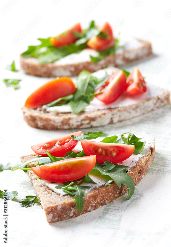 Tasty sandwiches with cream cheese, cherry tomatoes and fresh herbs. Bright wooden background. Close up.