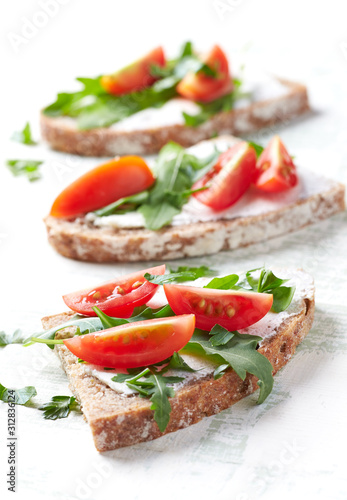 Tasty sandwiches with cream cheese, cherry tomatoes and fresh herbs. Bright wooden background. Close up.