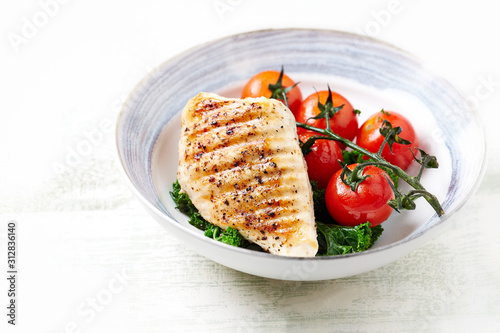 Grilled Chicken Breast with roasted Cherry Tomatoes. Bright wooden background. Close up. Copy space.