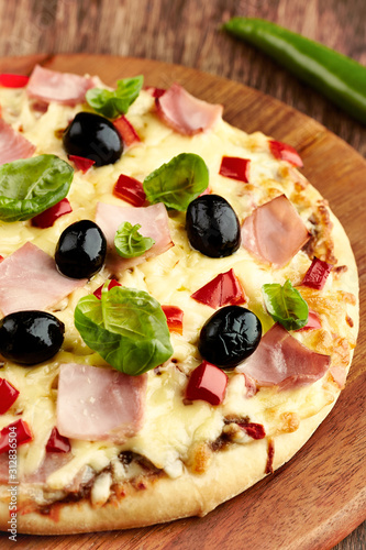 Pizza with ham, red pepper, black olives and fresh basil on rustic wooden background.