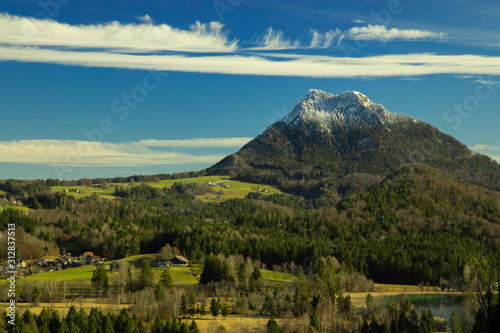 European village in Austrian Alps rural country side houses in spring time season green trees and meadows nature outdoor environment  lonely mountain snowy peak horizon background with blue sky