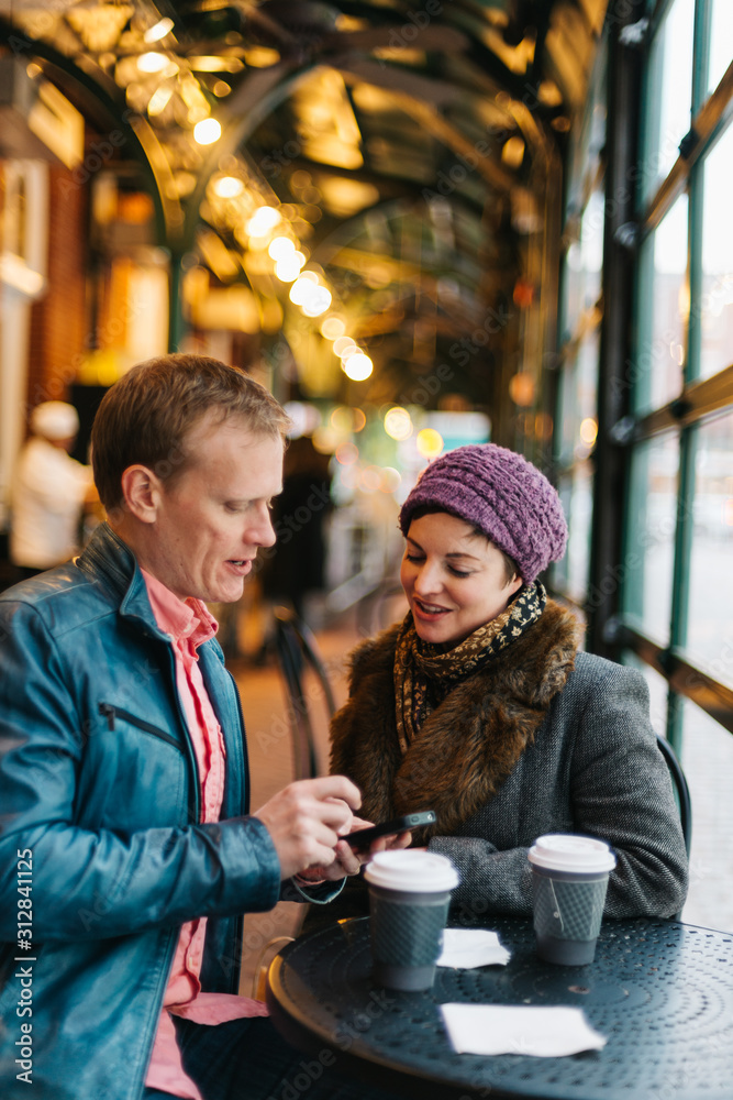 Caucasian couple sitting in a cafe drinking coffee and using a handheld smartphone device