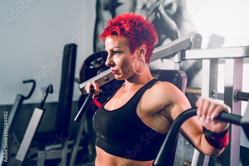 Young caucasian woman red hair athlete training at the gym working on chest pectoral muscles press on the machine fitness body building
