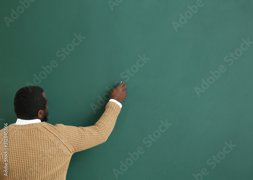 African-American teacher writing on blackboard in classroom