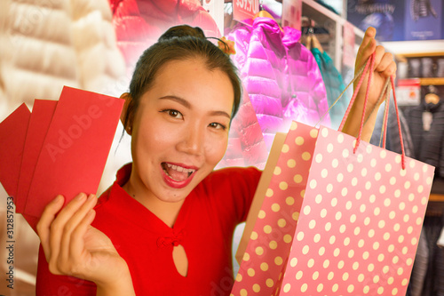 lifestyle portrait of young beautiful and happy Asian Chinese woman holding Chinese New year red pockets and shopping bags at modern shopping mall smiling excited spending money