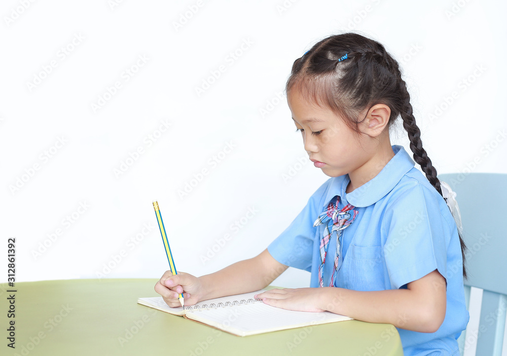 Intend little kid girl in school uniform writing on notebook at desk isolated over white background. Intend little kid girl in school uniform writing on notebook at desk isolated over white background.