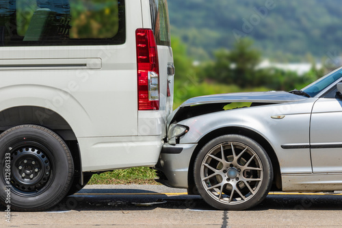 Car accident involving two cars on the road. Back side of van and front of siver car get damaged by accident photo