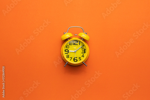 Fotografie Yellow alarm clock on the middle of orange background
