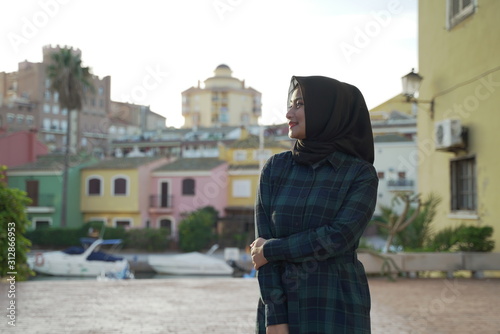 Asean young hijab girl smiling againts colorful Town houses and buildings in the town center of Valencia around port Saplaya