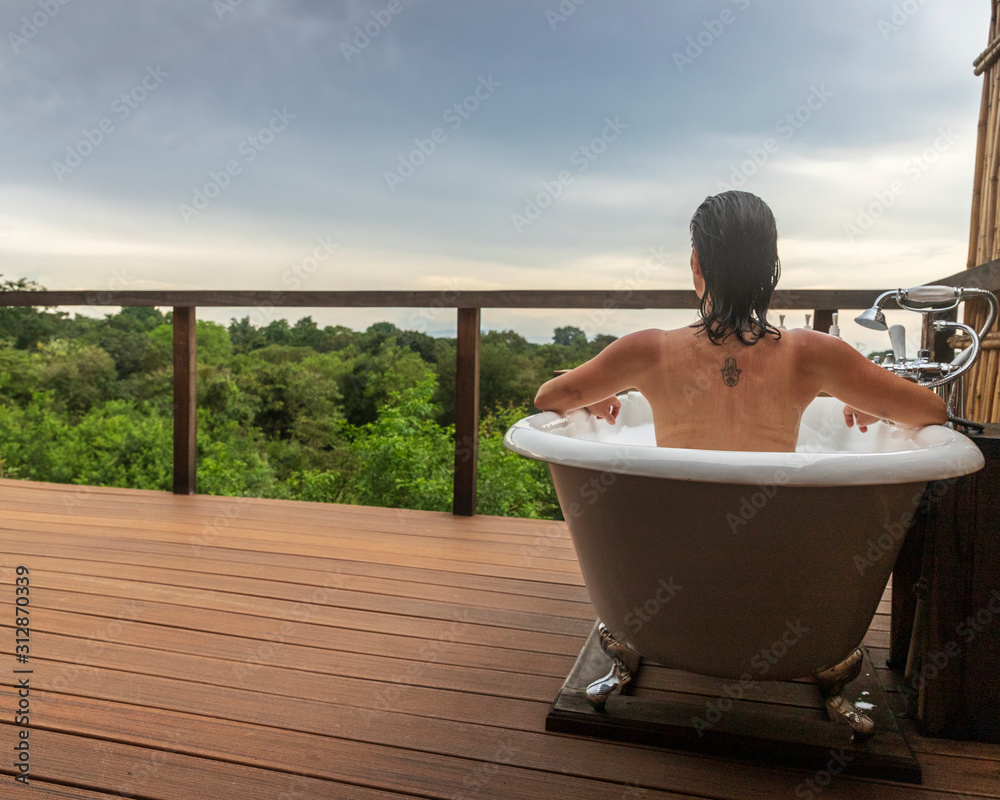Obraz na plátně Young woman enjoying a relaxing bubble bath on an outdoors bathtub with the forest as a background