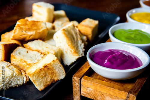 Delicious toasted bread on black dish served with varieties colorful dipping cream in white bowls on wooden table , most popular Thai dessert photo