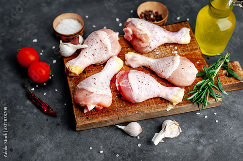  raw chicken legs with spices on a cutting board on a stone background