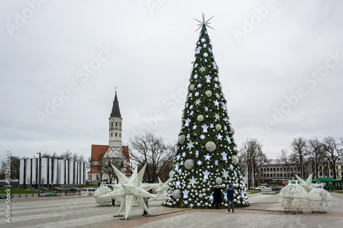 Siauliai, Lithuania - A Christmas tree in the square decorated with white balls, angels, stars and snowflakes, next to it are white installations of balls and stars, in the background is the cathedral